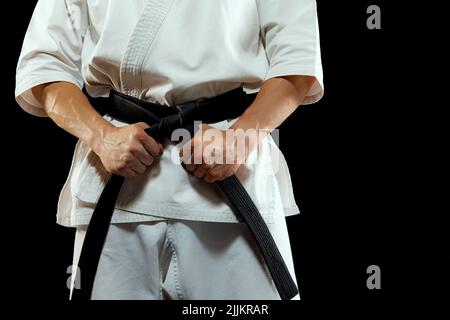 Image rognée d'un chasseur de karaté mâle dans un kimono blanc et ceinture noire en position de combat sur fond sombre. Sport, action, sports de combat, concept publicitaire Banque D'Images