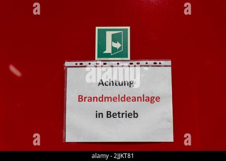 Une bannière « Avertissement système d'alarme incendie en fonctionnement » en allemand sur un mur rouge Banque D'Images
