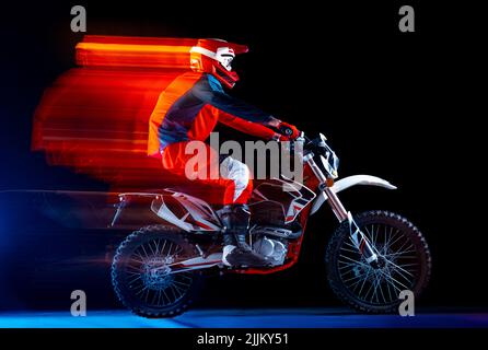 Portrait d'un jeune homme, motard à moto isolé sur fond noir au néon avec lumières mélangées. Debout sur la roue arrière Banque D'Images