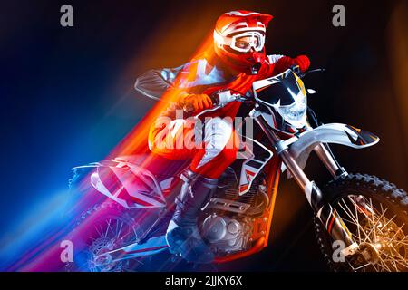 Portrait d'un jeune homme, motard à moto isolé sur fond noir au néon avec lumières mélangées. Accélérer le développement. Banque D'Images