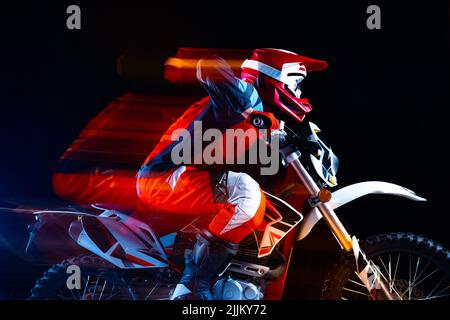 Portrait d'un jeune homme, motard à moto isolé sur fond noir au néon avec lumières mélangées Banque D'Images