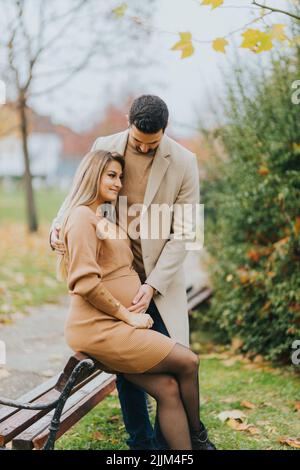 Une jeune femme enceinte et son mari se penchent sur un banc en bois Banque D'Images