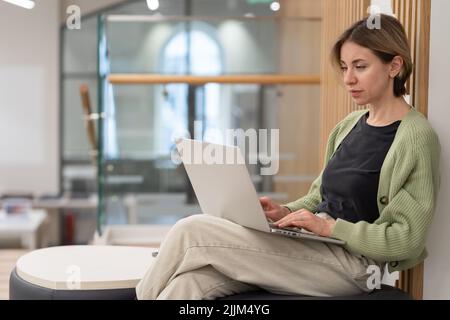 Femme d'âge moyen et pensive travaillant sur un ordinateur portable dans une bibliothèque Banque D'Images