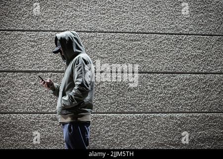 Vue latérale d'une personne dans un anorak tenant son téléphone contre un fond de mur rayé Banque D'Images
