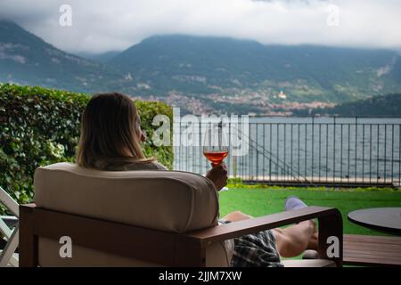 Femme se détendant et buvant Aperol Spritz en chaise, devant le lac de Côme en Italie Banque D'Images