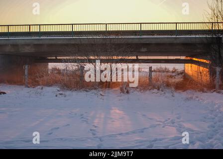 Vue panoramique sur le pont au-dessus d'un champ enneigé depuis un jardin au coucher du soleil Banque D'Images
