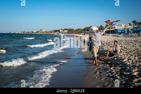 Un vendeur vendant des cerfs-volants et des chapeaux marche le long de la plage en fin d'après-midi près de Port El Kantaoui en Tunisie. Banque D'Images