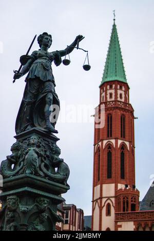 Un cliché vertical de la statue de la Dame de Justice et de l'église Saint-Nicolas à Francfort, en Allemagne Banque D'Images