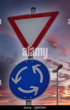 Une photo verticale des panneaux de signalisation de Yield et de Roundabout avec un magnifique fond de ciel coloré de coucher de soleil Banque D'Images