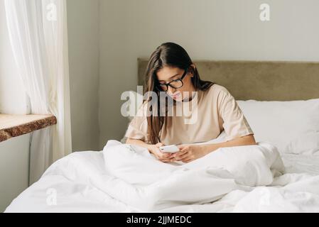 Dépendance moderne aux gadgets. La fille utilise immédiatement le téléphone après le réveil. Banque D'Images