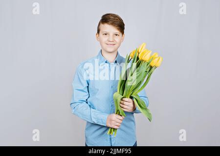 Jeune garçon adolescent avec des tulipes jaunes fleurs sur fond clair. Jeune garçon avec bouquet de fleurs Banque D'Images