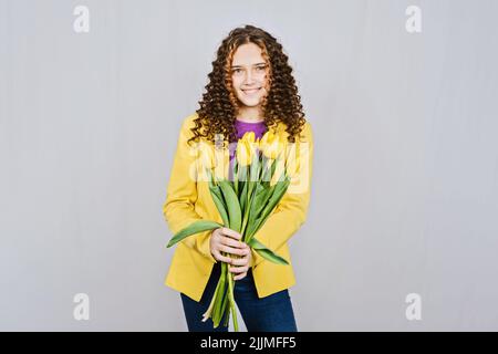 Jeune fille adolescente avec des tulipes jaunes fleurs sur le fond clair. Jeune fille avec bouquet de fleurs Banque D'Images