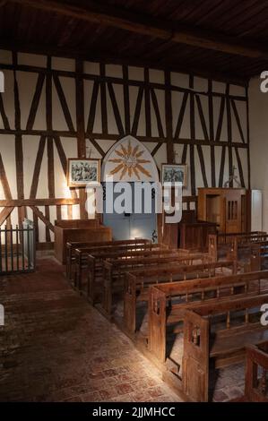 Des ragoûts en bois fonctionnels et un ancien pavé rouge rehaussent l'atmosphère rustique à l'intérieur de l'église notre-Dame à colombages, construite au début de 1500s à Châtillon-sur-Broué dans la Marne, au Grand est, en France. Dans cette vue de l'extrémité ouest de la nef, les portes doubles grises menant à une rare véranda entièrement fermée sont flanquées d'un stand confessionnel et d'une ancienne boîte en bois pew. Banque D'Images