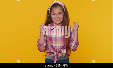 Jeune enfant préadolescent fille criant, levant des poings dans le geste je l'ai fait, célébrant le succès, gagnant, anniversaire, succès de loterie. Petits enfants isolés sur fond jaune studio Banque D'Images