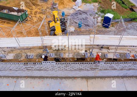 Pendant que les ouvriers du bâtiment travaillent sur des échafaudages, ils posent des blocs de béton pour cinder la maçonnerie Banque D'Images