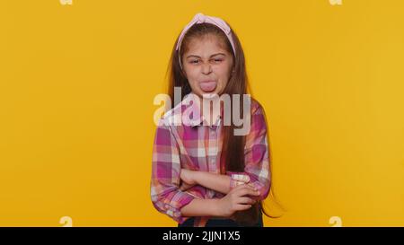 Joyeux drôle jeune enfant jeune fille de préadolescence montrant la langue faire des visages à la caméra, se tromper autour, plaisantant, en apantant avec le visage stupide, taquinerie. Petits enfants isolés sur fond jaune studio Banque D'Images