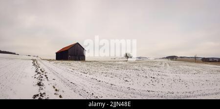 Une vue panoramique d'une grange en bois un champ couvert de neige sous un ciel bleu sans nuages au coucher du soleil Banque D'Images
