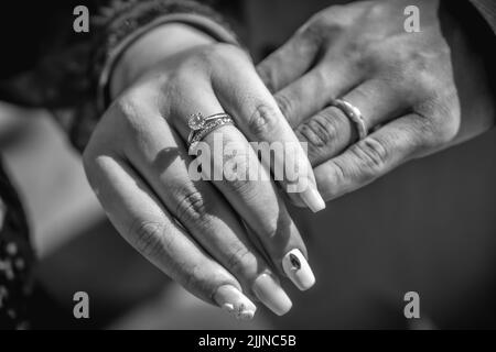 Un gros plan en niveaux de gris des mains de la jeune mariée et du marié avec les anneaux. Banque D'Images