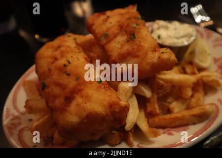 Un gros plan d'un plat de poisson et de croustilles avec une sauce tartare et du citron Banque D'Images