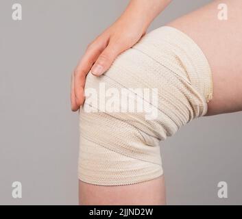 Une femme enroule un bandage de compression autour d'un genou douloureux pour soulager la douleur ou prévenir les blessures. Entorses musculaires, foulures, traitement de la surutilisation. Problèmes de santé, conditions médicales. Photo de haute qualité Banque D'Images