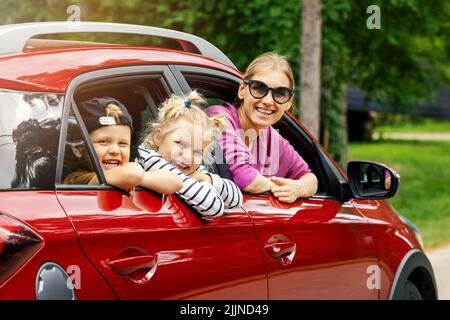 voyage en famille. mère avec des enfants souriant et s'inclinant hors de la fenêtre de la voiture Banque D'Images