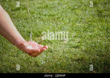 Un gros plan d'eau pure qui coule sur une main avec de l'herbe verte en arrière-plan, copier l'espace Banque D'Images