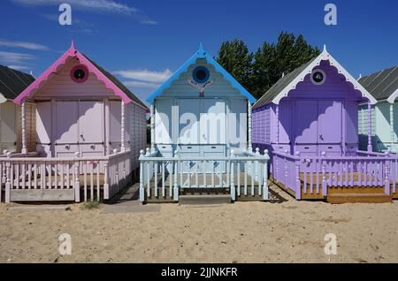 Cabanes de plage aux couleurs vives sur l'île de Mersea, Essex. Cabanes en bois pastel dans une rangée, avec un ciel bleu. Banque D'Images