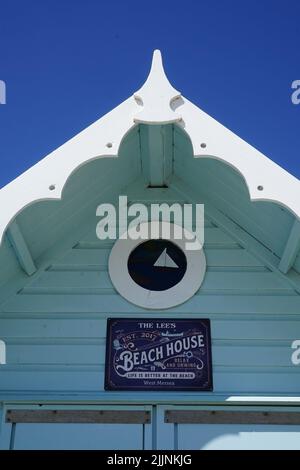 Gros plan : cabane de plage en bois bleu clair 'Blue Breeze' sur l'île de Mersea, Essex. Extrémité de pignon avec fenêtre ronde et signe de nom de mouette. Banque D'Images