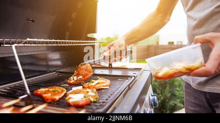 Une main jeune fait griller quelques brochettes de viande et de légumes sur un énorme gril à gaz, concept alimentaire Banque D'Images