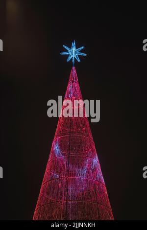 Une photo verticale de l'arbre de Noël illuminé en rouge, surmontée d'une étoile bleue contre le ciel nocturne Banque D'Images