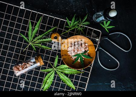 Vue en hauteur des feuilles de marijuana et du sel himalayan rose dans des pots de verre sur une roche de refroidissement métallique Banque D'Images