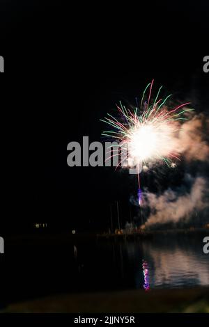 Une vue fascinante sur le feu d'artifice au-dessus de la ville et de l'eau du lac tard dans la nuit Banque D'Images