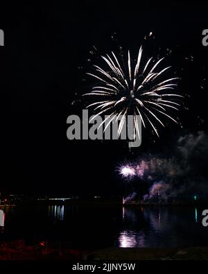 Une vue fascinante sur le feu d'artifice au-dessus de la ville et de l'eau du lac tard dans la nuit Banque D'Images