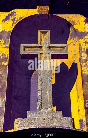 Ancienne croix en pierre sculptée dans la niche de l'église - stylisée en jaunes et violets avec ombre Banque D'Images