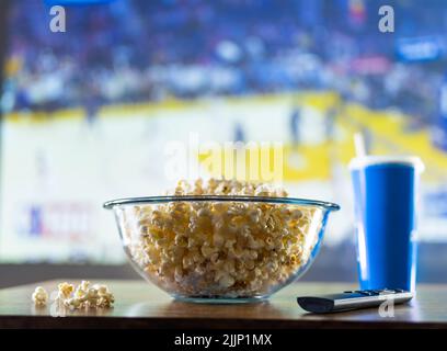 L'ensemble traditionnel d'un fan de sport est un grand bol en verre de pop-corn, une boisson gazeuse et une télécommande de télévision sur fond d'un match de basket-ball sur la TV Banque D'Images