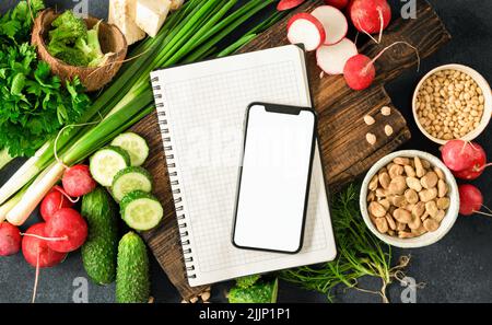 Commander des aliments en ligne téléphone mobile avec écran vierge, bloc-notes et légumes frais, herbes, céréales et noix Banque D'Images