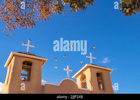 Pigeons volant au-dessus du toit et des clochers de la célèbre église de mission adobe San Francisco de Asis sur la place principale de Ranchos de Taos, Nouveau-Mexique Banque D'Images