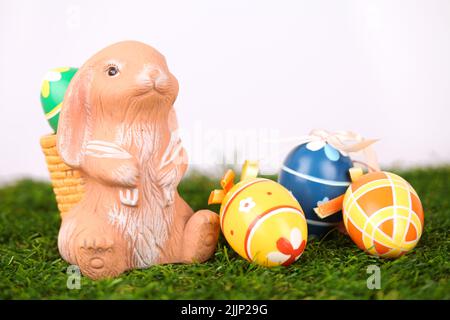 Trois oeufs peints et une figurine de lapin avec un panier sur son dos sur l'herbe - fond de Pâques Banque D'Images