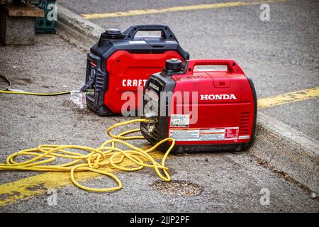 Générateurs portables Red et Black Honda et Craftsman installés dans le parking avec des cordons menant à ce qui est chargé. La location est peinte sur le Banque D'Images