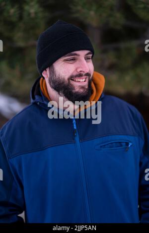 Une photo verticale d'un jeune homme caucasien dans une veste d'hiver bleue debout dans un parc et souriant Banque D'Images