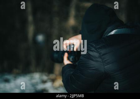Vue arrière d'un photographe prenant des photos à l'aide d'un appareil photo numérique sur un arrière-plan flou Banque D'Images
