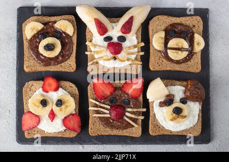 Toasts amusants avec tartiner au chocolat, fromage à la crème, fraises, bananes et raisins secs. Petit déjeuner pour les enfants Banque D'Images