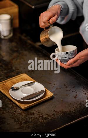 Un cliché vertical d'une femme qui verse du lait dans une tasse dans un café pendant sa pause-café Banque D'Images