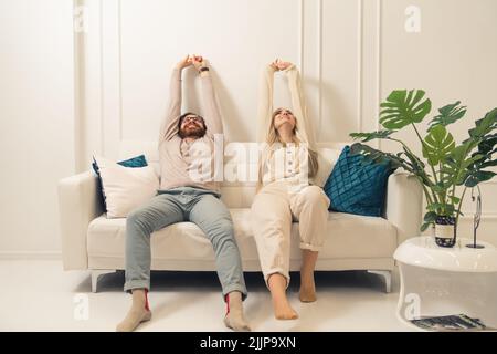 Couple caucasien assis sur un canapé blanc dans la salle de séjour avec les mains vers le haut et les traînées ensemble. Prise de vue en intérieur. Photo de haute qualité Banque D'Images