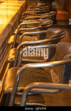 Tabourets de bar en cuir usés alignés sur un bar avec de la lumière qui brille sur lui dans une pièce sombre sélectif foyer Banque D'Images