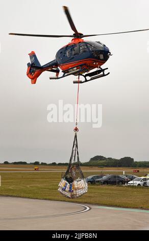 Cornwall, Angleterre, Royaume-Uni. 2022. Hélicoptère de transport aérien avec sangle de transport et porte-bagages à filet au-dessus d'un aérodrome de Cornish sur une opération de collecte et de livraison Banque D'Images