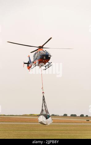 Cornwall, Angleterre, Royaume-Uni. 2022. Hélicoptère de transport aérien avec sangle de transport et porte-bagages à filet au-dessus d'un aérodrome de Cornish sur une opération de collecte et de livraison Banque D'Images