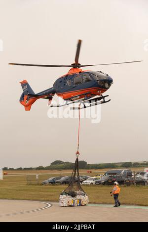 Cornwall, Angleterre, Royaume-Uni. 2022. Hélicoptère de transport aérien avec sangle de transport et porte-bagages à filet au-dessus d'un aérodrome de Cornish sur une opération de collecte et de livraison Banque D'Images