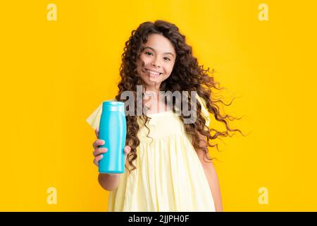 Portrait heureux de l'enfant jeune fille avec des shampooings et gel douche. Soins capillaires longs de l'adolescent. Présentation du produit cosmétique, bouteille de shampooing Banque D'Images