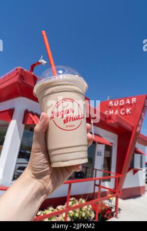 Rudyard, Montana - 2 juillet 2022 : la main tient un cocktail de chocolat au restaurant Sugar Shack du restaurant rétro à l'arrière-plan sur la chaîne (ou US-2) Banque D'Images